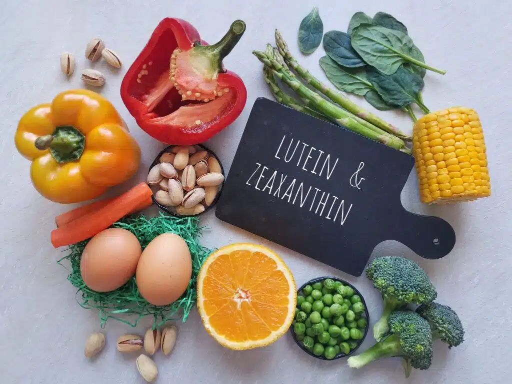 Various colorful vegetables and nuts rich in lutein and zeaxanthin displayed around a cutting board.